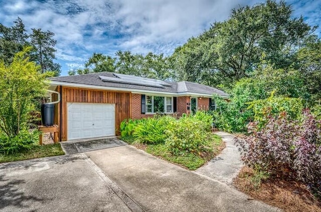 ranch-style house featuring concrete driveway, roof mounted solar panels, and a garage