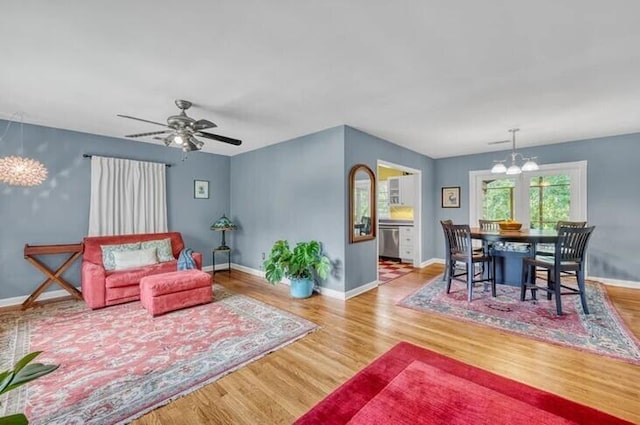 living area with baseboards, wood finished floors, and ceiling fan with notable chandelier