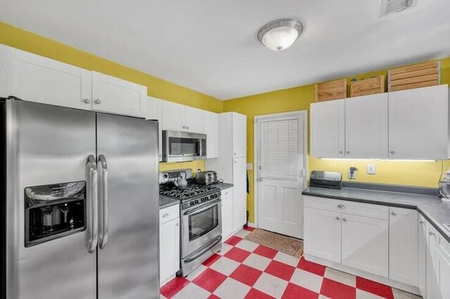 kitchen with dark countertops, light floors, appliances with stainless steel finishes, white cabinetry, and visible vents