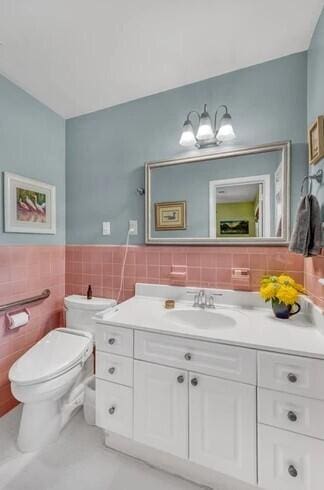 bathroom with tile walls, a wainscoted wall, vanity, and toilet