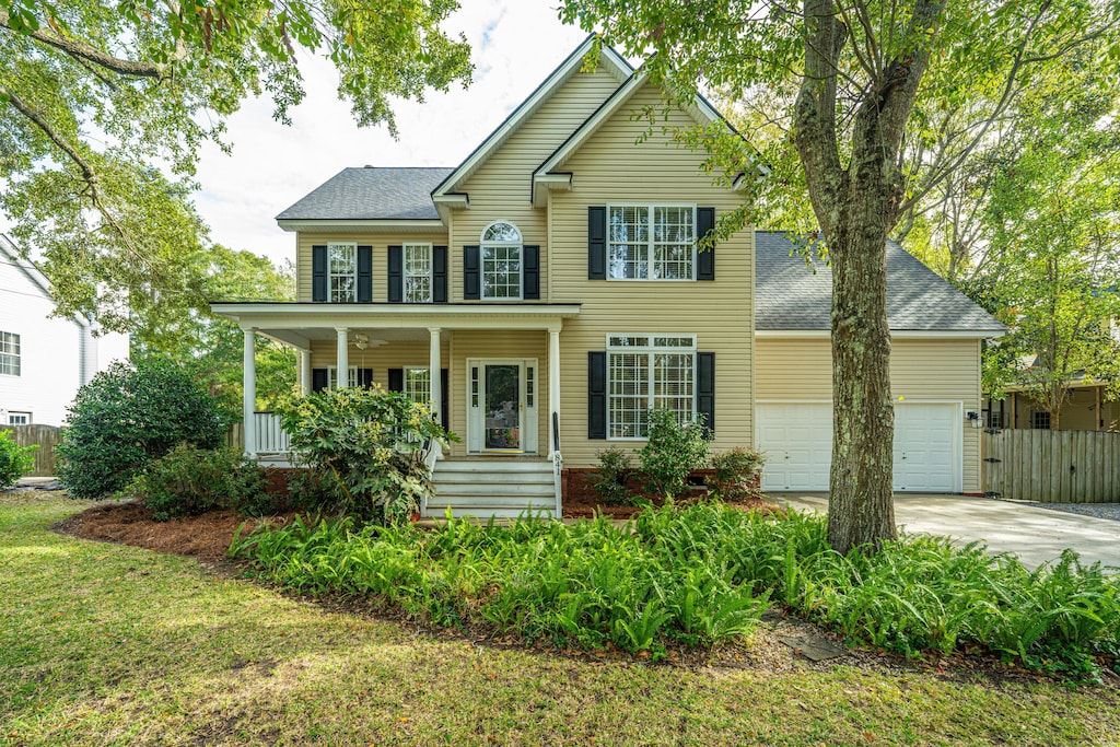 colonial house featuring covered porch, a garage, and a front yard