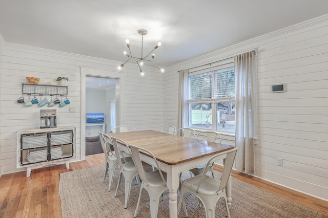 dining space featuring hardwood / wood-style flooring, wood walls, crown molding, and an inviting chandelier