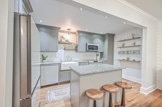 kitchen featuring gray cabinetry, light stone countertops, a center island, stainless steel appliances, and tasteful backsplash