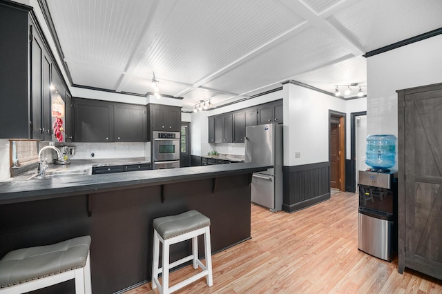 kitchen with sink, a breakfast bar area, appliances with stainless steel finishes, kitchen peninsula, and light wood-type flooring