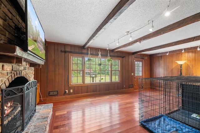 living room with beam ceiling, wooden walls, a fireplace, wood-type flooring, and a textured ceiling