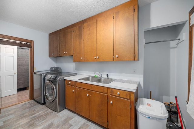 laundry room with sink, washing machine and dryer, cabinets, a textured ceiling, and light wood-type flooring