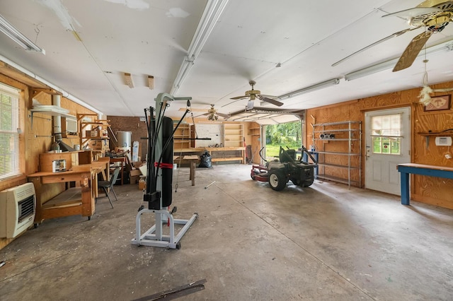 misc room with a workshop area, ceiling fan, wooden walls, concrete flooring, and heating unit