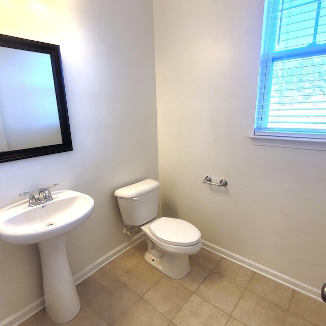 half bath with a sink, tile patterned flooring, toilet, and baseboards