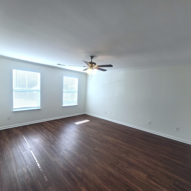 spare room with a ceiling fan, visible vents, baseboards, and dark wood-style flooring