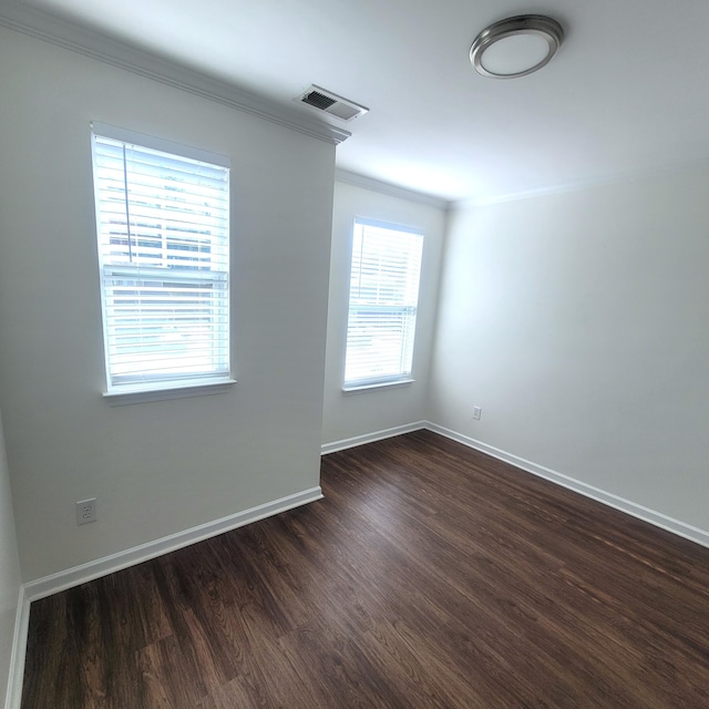 spare room with baseboards, visible vents, dark wood-type flooring, and ornamental molding