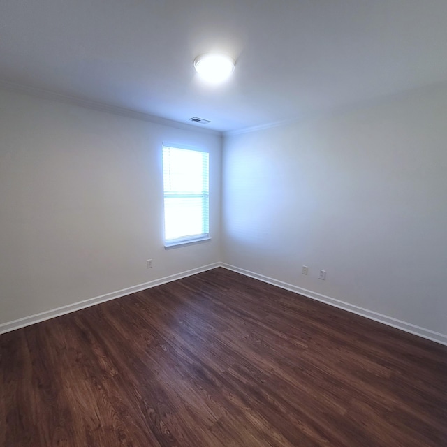 empty room featuring baseboards, dark wood-style flooring, visible vents, and crown molding