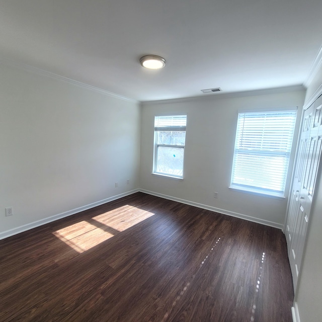 unfurnished room featuring dark wood-style floors, visible vents, baseboards, and crown molding