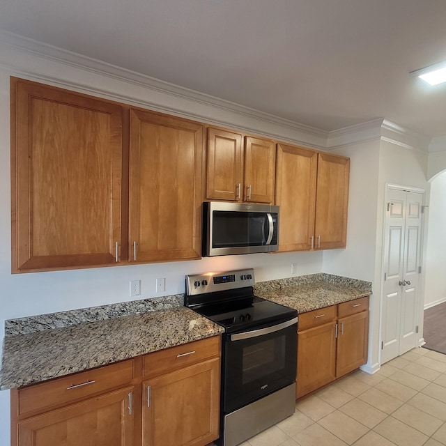 kitchen with stone countertops, light tile patterned flooring, appliances with stainless steel finishes, brown cabinetry, and crown molding