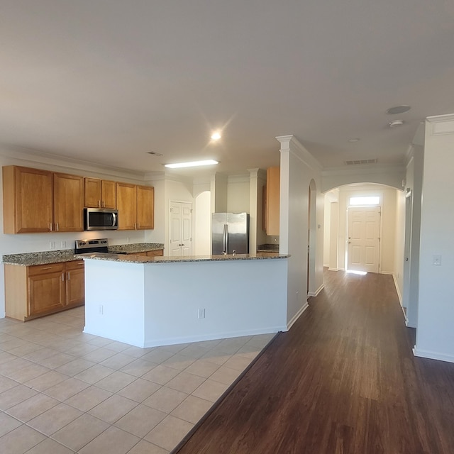 kitchen featuring arched walkways, visible vents, appliances with stainless steel finishes, ornamental molding, and dark stone counters