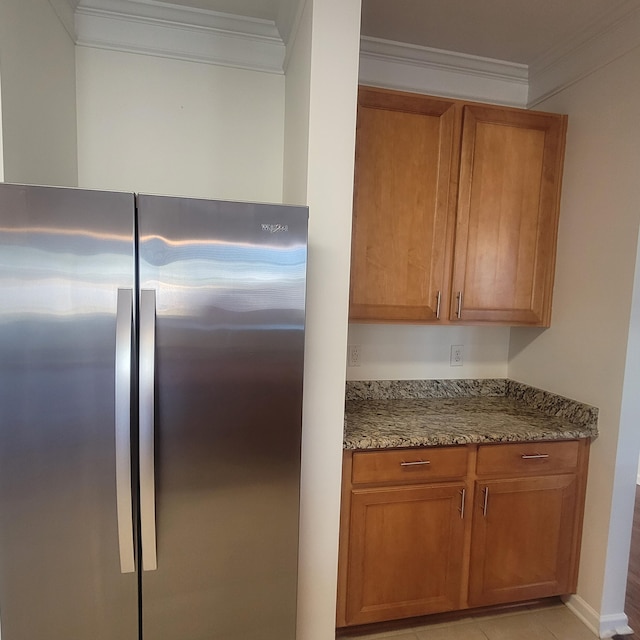 kitchen with ornamental molding, brown cabinetry, stone countertops, and freestanding refrigerator