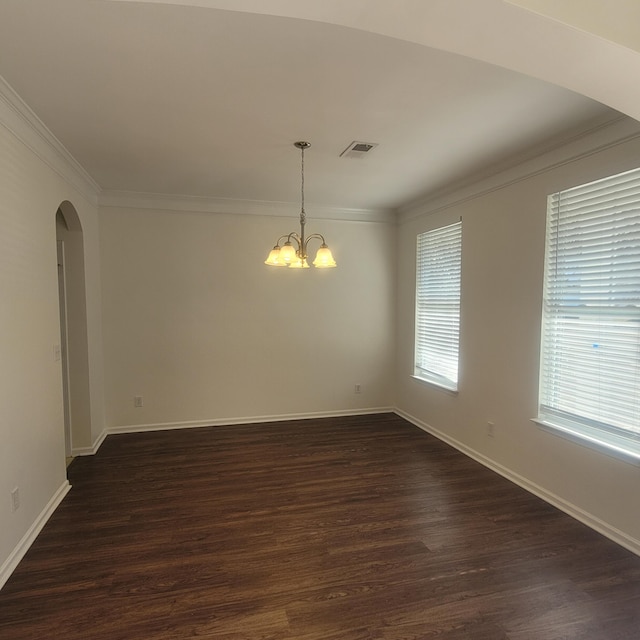 empty room with arched walkways, dark wood finished floors, visible vents, and crown molding