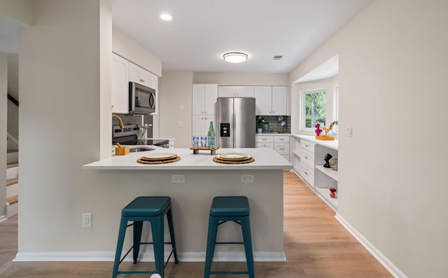 1478 Diamond Blvd, Mount Pleasant, SC 29466 - kitchen featuring appliances with stainless steel finishes, a kitchen bar, a peninsula, decorative backsplash, and white cabinetry