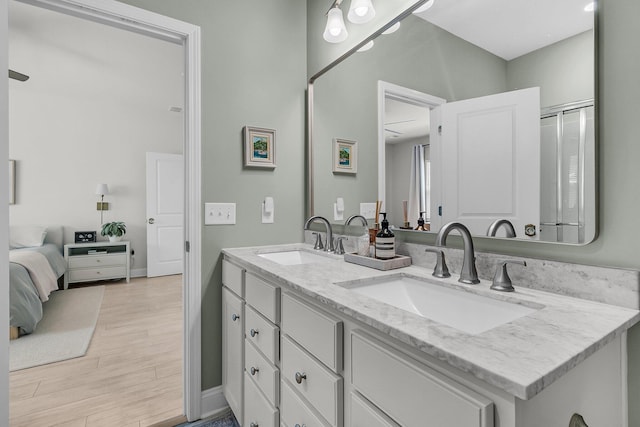 full bath with double vanity, a sink, baseboards, and wood finished floors