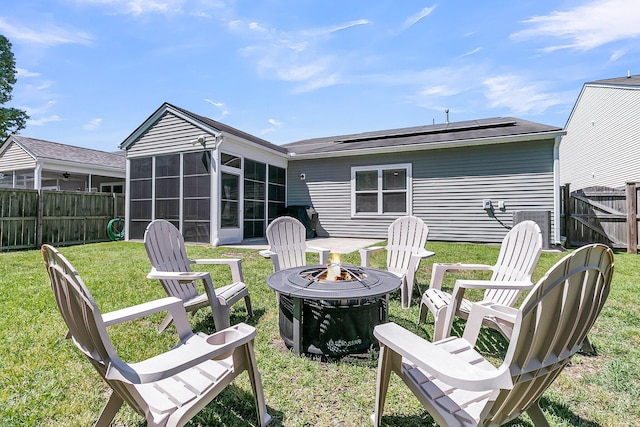rear view of house featuring a fire pit, a fenced backyard, a sunroom, a yard, and solar panels