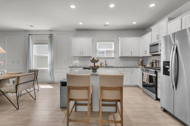 kitchen with a kitchen island, white cabinets, tasteful backsplash, a sink, and stainless steel appliances