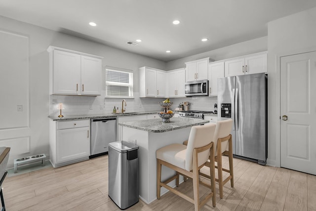 kitchen featuring appliances with stainless steel finishes, a sink, light wood finished floors, decorative backsplash, and a kitchen island