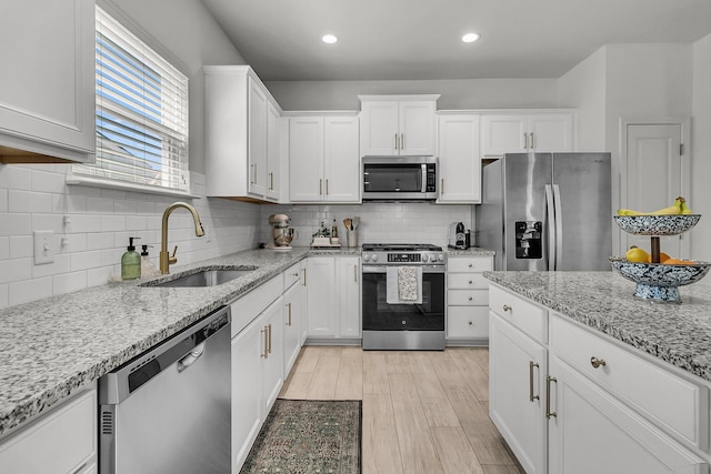 kitchen featuring decorative backsplash, white cabinets, a sink, light wood finished floors, and appliances with stainless steel finishes