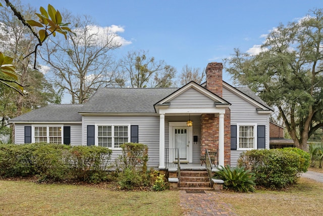 bungalow-style house with a shingled roof, a chimney, and a front yard