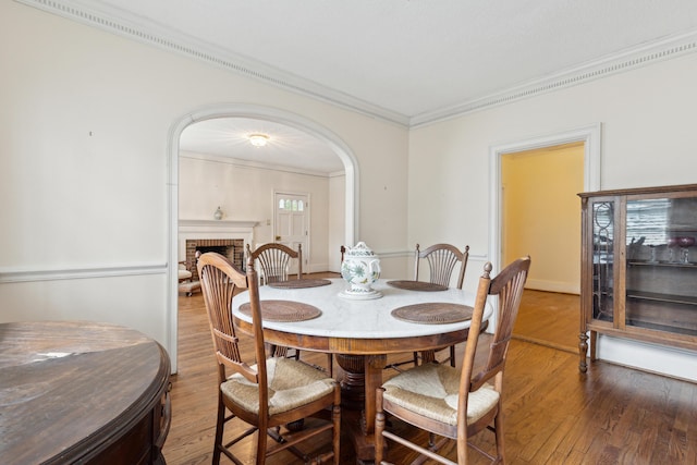 dining area with a brick fireplace, crown molding, arched walkways, and wood finished floors