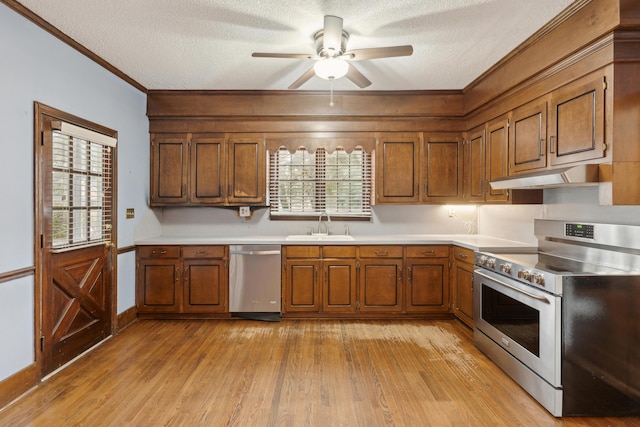 kitchen featuring appliances with stainless steel finishes, brown cabinets, light countertops, under cabinet range hood, and a sink