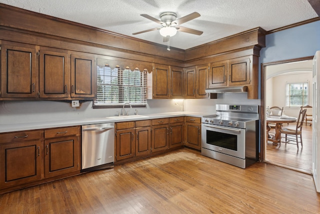 kitchen featuring stainless steel appliances, light countertops, brown cabinetry, a sink, and light wood-type flooring