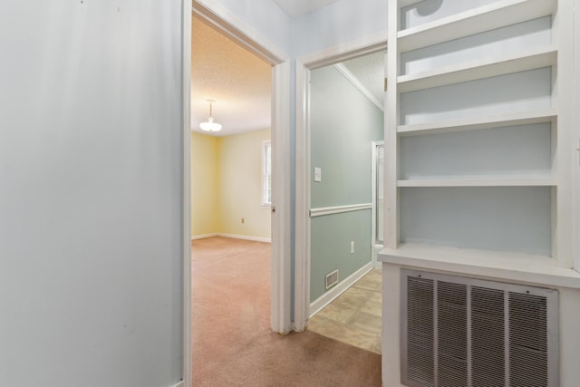 hallway with light carpet, baseboards, visible vents, and a textured ceiling