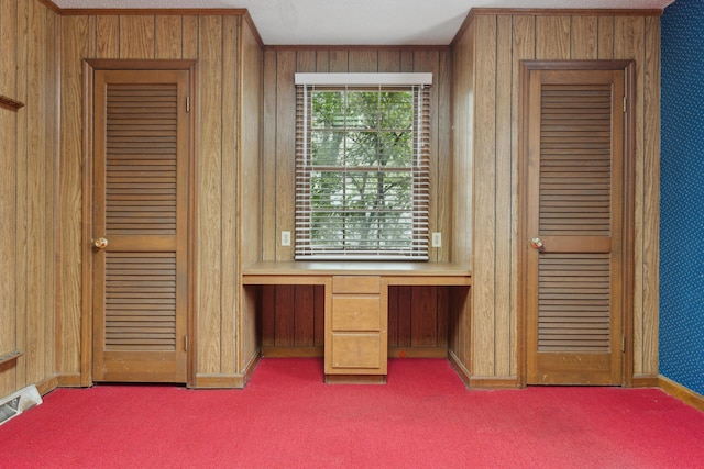 unfurnished office featuring wood walls, visible vents, built in desk, and carpet flooring