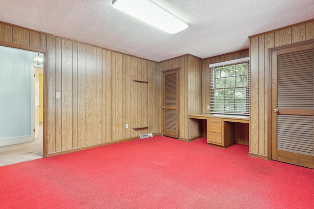 interior space with carpet floors, wooden walls, built in desk, and a textured ceiling