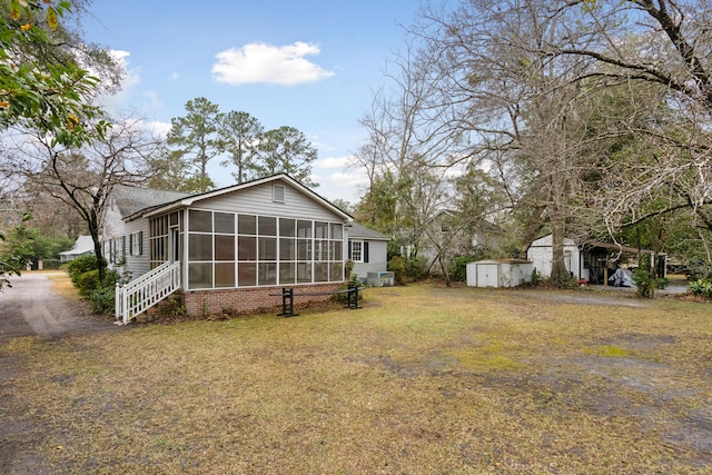 rear view of property with a sunroom, a lawn, an outdoor structure, and a storage unit