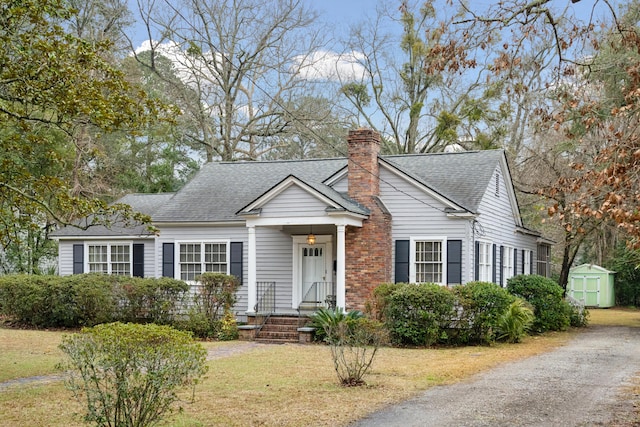 view of front of house with an outdoor structure, roof with shingles, a storage unit, a chimney, and a front yard