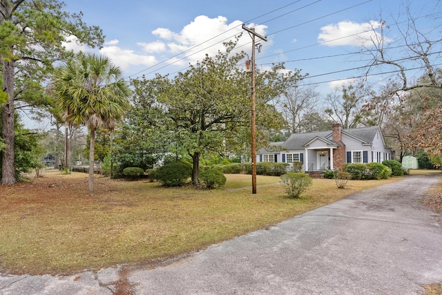 view of front facade featuring driveway, a chimney, and a front yard