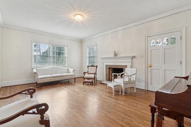 living area featuring baseboards, wood finished floors, crown molding, a textured ceiling, and a brick fireplace