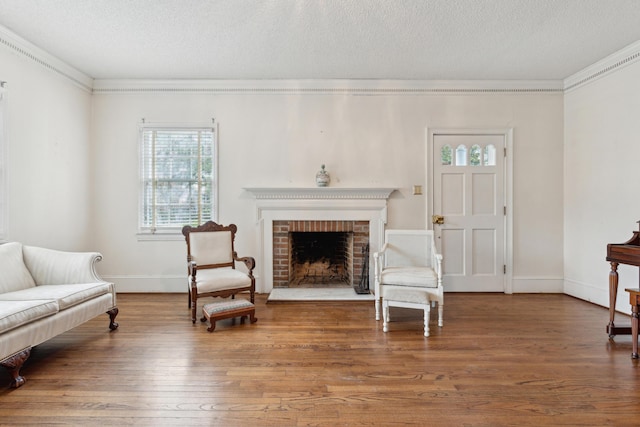 living area featuring a textured ceiling, ornamental molding, a brick fireplace, and wood finished floors