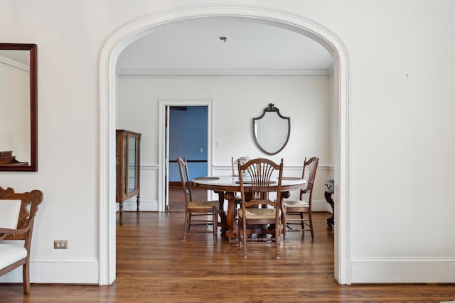 dining area featuring arched walkways, dark wood-type flooring, ornamental molding, and baseboards