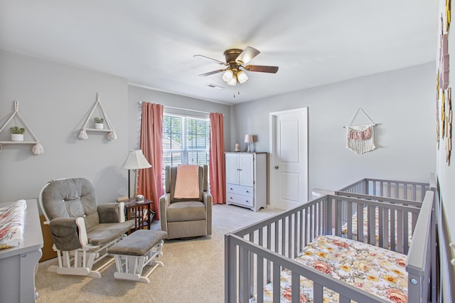 bedroom featuring a nursery area, ceiling fan, and light colored carpet