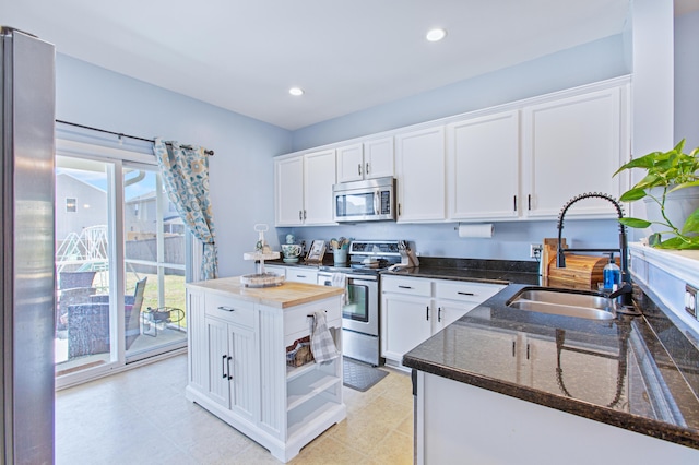 kitchen featuring appliances with stainless steel finishes, dark stone countertops, white cabinetry, a sink, and recessed lighting