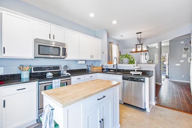 kitchen featuring butcher block countertops, appliances with stainless steel finishes, a peninsula, white cabinetry, and a sink