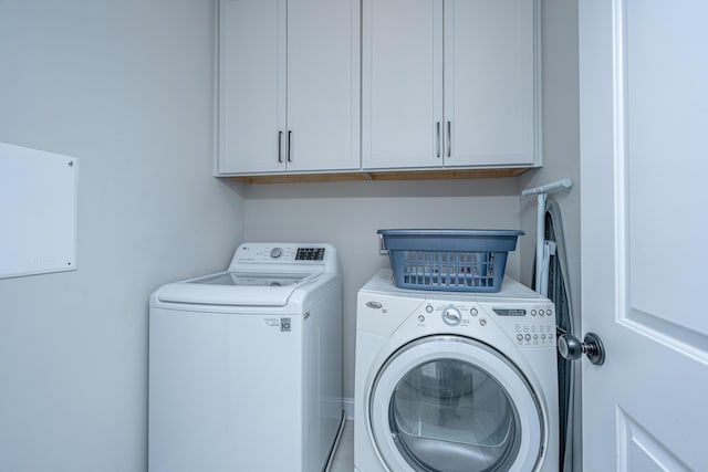 clothes washing area with separate washer and dryer and cabinets