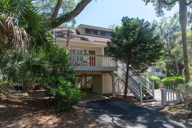 coastal home featuring covered porch, stairs, roof with shingles, and asphalt driveway