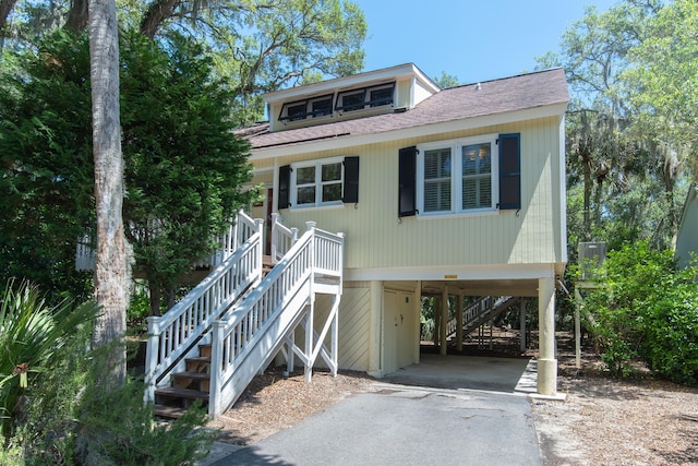 beach home with stairs, a carport, driveway, and roof with shingles