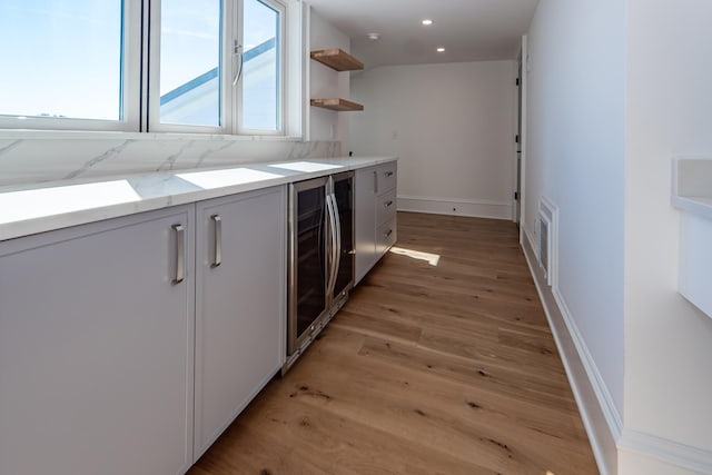 kitchen with backsplash, wine cooler, light stone counters, and light wood-type flooring