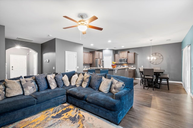 living area featuring ceiling fan with notable chandelier, recessed lighting, arched walkways, baseboards, and dark wood-style flooring