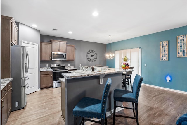 kitchen with a breakfast bar area, baseboards, light wood finished floors, a center island with sink, and appliances with stainless steel finishes