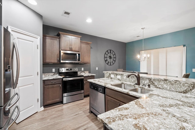 kitchen featuring decorative light fixtures, a chandelier, light wood-style flooring, stainless steel appliances, and a sink