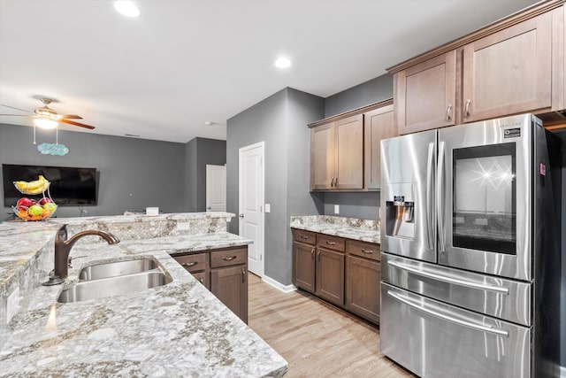 kitchen with light stone counters, a ceiling fan, light wood-style flooring, a sink, and stainless steel refrigerator with ice dispenser